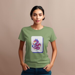 May include: A light green t-shirt featuring a white rectangle with a colorful dragon illustration. The dragon is red, blue, and purple. The t-shirt is made of a soft material.