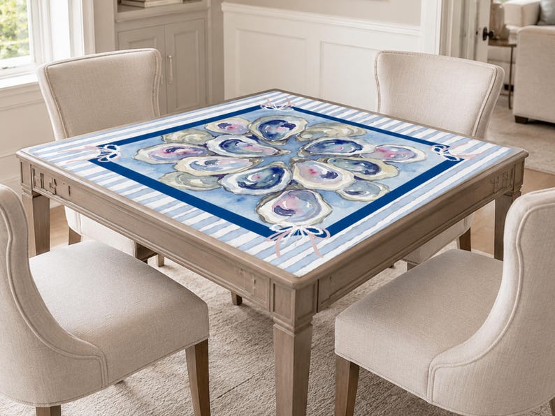 May include: A square wooden table with a watercolor oyster design on the tabletop. The design features blue, purple, and white oyster shells arranged in a circular pattern on a blue background with blue and white stripes. Four beige chairs surround the table.
