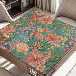 May include: A wooden table with a teal surface featuring a tropical design. The design includes pink hibiscus flowers, sea creatures like turtles and seahorses, and coral. The table is surrounded by two grey chairs.
