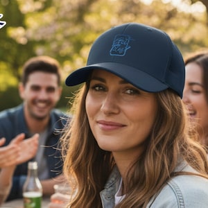 Op de afbeelding: Marineblauwe baseballcap met een gebogen klep en mesh achterkant. De cap heeft een tonale geborduurde opdruk op de voorkant. De afbeelding toont een groep mensen buiten, met de cap gedragen door een persoon op de voorgrond.