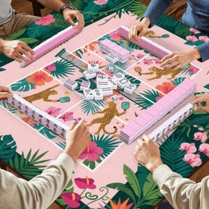 May include: A group of people playing Mahjong on a table with a pink floral and leopard print design. The game pieces are white and pink. The table is surrounded by green tropical leaves and pink flowers.
