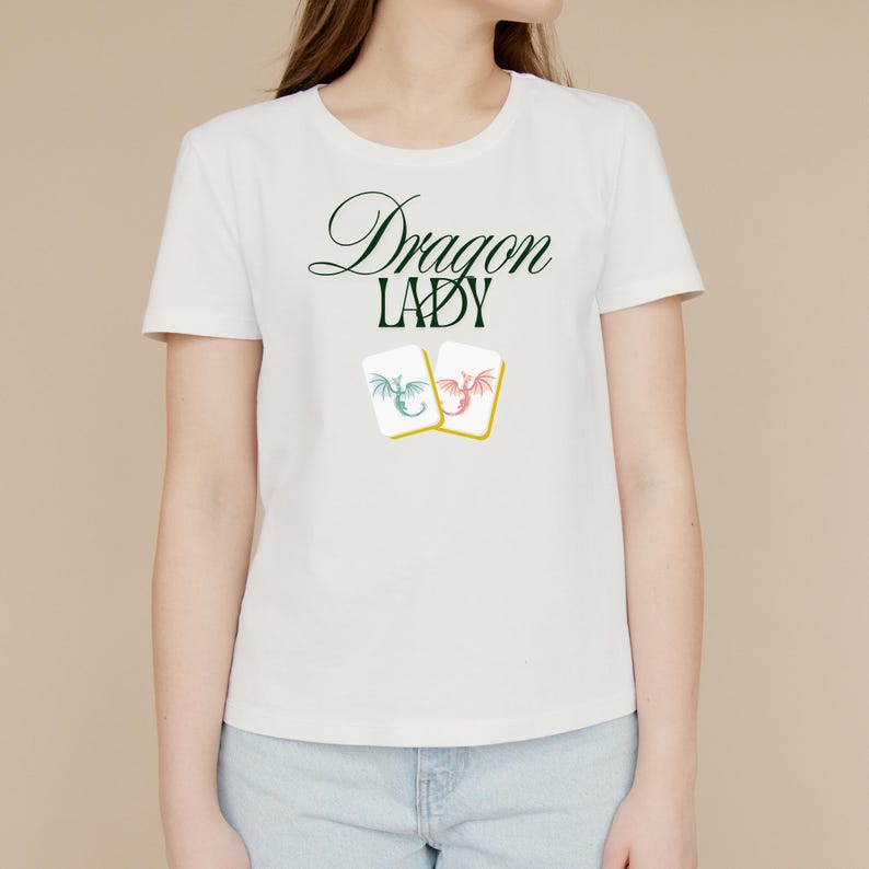 May include: White t-shirt with the text "Dragon Lady" in green and black script. Below the text are two small cards with dragon illustrations in blue and red. The shirt is a crew neck style.