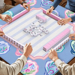 Puede incluir: Una partida de Mahjong en curso, con jugadores alrededor de una mesa. La mesa tiene un patr&oacute;n floral azul claro. Se ven estanter&iacute;as rosas y fichas blancas. Los jugadores sostienen las fichas y las estanter&iacute;as.