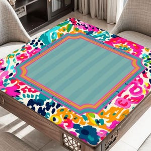 May include: A wooden table with a colorful floral patterned top. The top features a central light blue section with vertical stripes, framed by a decorative border. The floral pattern includes pink, blue, and yellow accents.
