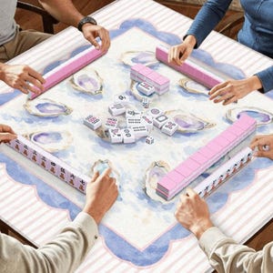 May include: A group of people playing Mahjong. The game is set on a square table with a light blue and white patterned surface. Pink tiles and racks are visible, along with other game pieces.