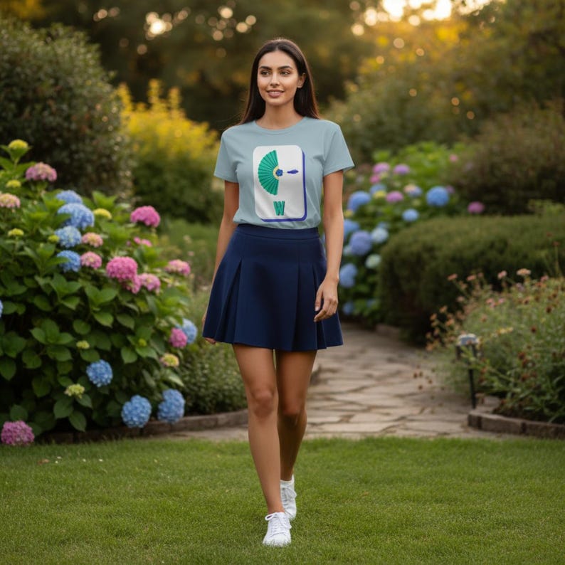 May include: A light blue t-shirt with a graphic design featuring a teal and white image with the letter "W" is paired with a navy blue pleated skirt. The person is wearing white sneakers and walking on a grassy path.