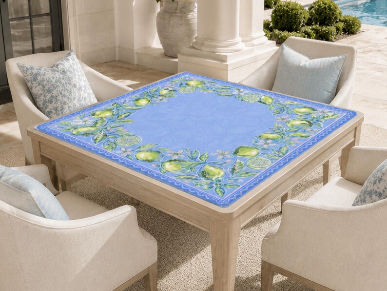 May include: A square wooden table with a light blue surface, adorned with a border of green lemons and white flowers. The table is surrounded by four cream-colored chairs with light blue pillows. The table is approximately 40 inches square.