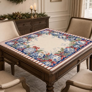 May include: A square tablecloth featuring a cream-coloured centre and a decorative border. The border displays blue and white patterned ornaments, green pine branches, red berries, and red ribbons, finished with a red and white striped edge.