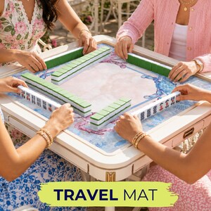 May include: A group of people playing Mahjong on a white and beige table with green and white tiles. The table has a blue and white patterned surface. The text "TRAVEL MAT" is displayed on a green and yellow banner.