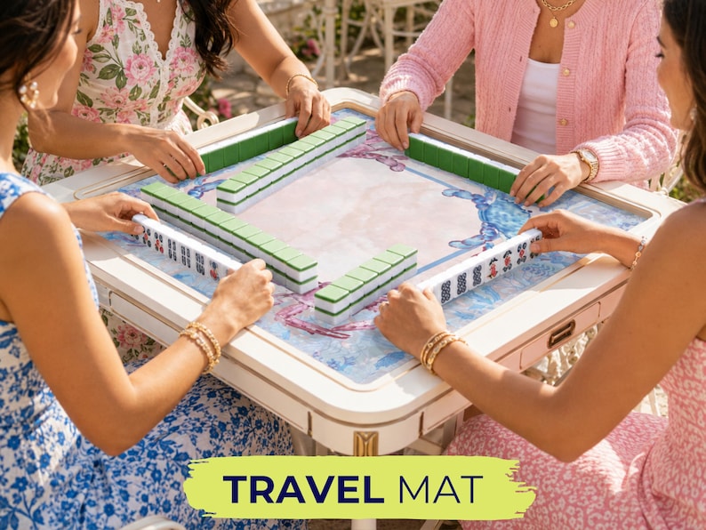 May include: A group of people playing Mahjong on a white and beige table with green and white tiles. The table has a blue and white patterned surface. The text "TRAVEL MAT" is displayed on a green and yellow banner.
