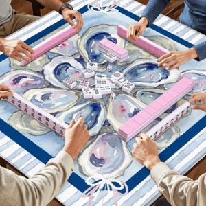 May include: A group of people playing Mahjong. The game is set on a table with a blue and white oyster-themed design. Pink tile racks and white tiles are visible, with players' hands around the table.
