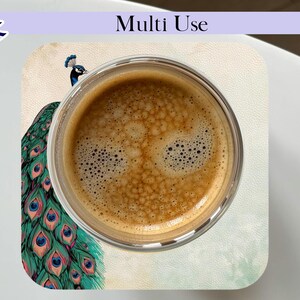 May include: A clear glass cup filled with coffee sits on a coaster. The coaster features a peacock design with teal, blue, and gold feathers. The words "Multi Use" are printed on the top of the image.