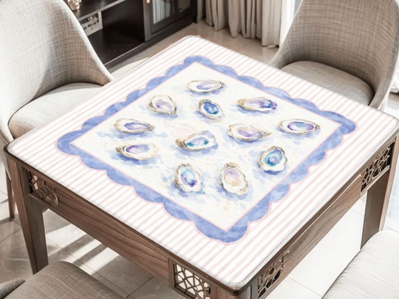 May include: A wooden table with a white and pink striped surface. The table has a square, scalloped blue border with watercolor oyster shell illustrations. The table is surrounded by two chairs.
