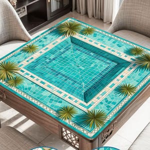May include: A square wooden table with a turquoise mosaic tile design resembling a swimming pool. The table has a dark wood frame and is surrounded by chairs. Green palm frond accents are placed around the pool design.