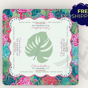 May include: Square decorative item with a tropical floral design in shades of pink, teal, and green. The center features a large, light green monstera leaf. Text includes "Charleston" and other phrases.