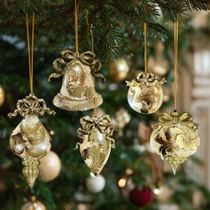 May include: Five gold-toned glass Christmas ornaments hanging from thin strings. The ornaments feature intricate swirling patterns, metallic finishes, and decorative bow-shaped toppers. The shapes include a bell, a teardrop, and three round baubles.