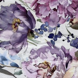 May include: A white paper napkin featuring a watercolor-style floral pattern with large, layered peony blossoms in shades of deep purple, lavender, and soft pink, accented by small blue flower clusters and green foliage on a textured surface.