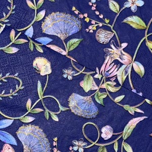 May include: A dark navy blue paper napkin featuring a repeating botanical pattern of light blue and purple fan-shaped flowers, delicate green vines, and small white blossoms. The design includes soft pastel highlights and intricate floral details.