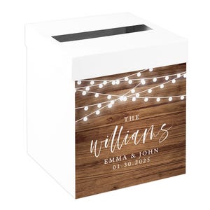 May include: A white card box with a slot on top. The front features a wood-grain design with string lights and the names "The Williams" and "EMMA & JOHN 01.30.2025" in white script.