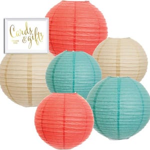 May include: A collection of colorful paper lanterns in coral, teal, and cream. A framed sign with gold lettering reads "Cards & Gifts Thank You". These decorative lanterns are ideal for parties and events.