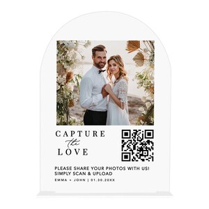 May include: A white wedding sign with an arched top. The sign features a photo of a couple and the words "CAPTURE the LOVE". It includes a QR code and the text "PLEASE SHARE YOUR PHOTOS WITH US! SIMPLY SCAN & UPLOAD".