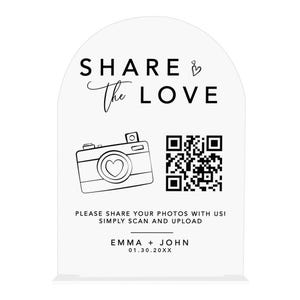 May include: A white acrylic wedding sign with an arched top. The sign features the text "SHARE the LOVE" and a camera graphic with a heart-shaped lens. Includes a QR code and the text "PLEASE SHARE YOUR PHOTOS WITH US! SIMPLY SCAN AND UPLOAD".