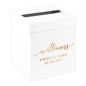 May include: A white card box with a slot on top for cards. The box has gold lettering that reads "williams" above "EMMA & JOHN" and the date "01.30.2025". The box is likely for a wedding or special event.