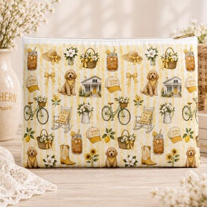 May include: A rectangular zipped pouch featuring a repeating pattern on a yellow and white striped background. The print includes illustrations of golden retriever puppies, bicycles, rocking chairs, cowboy boots, sun hats, lemons, and flowers.