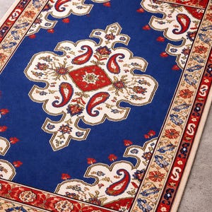 May include: A rectangular rug with a central blue field featuring a white and red paisley design. The border is red and beige with floral patterns. The rug has a traditional, ornate style.