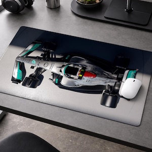 May include: A computer mouse and a mousepad featuring a Formula 1 race car. The mousepad has a silver, black, and teal design of the car. A white mouse is on the right side of the pad.