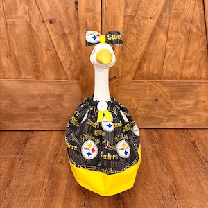 May include: A decorative goose dressed in a black and yellow Pittsburgh Steelers outfit. The outfit includes a bow, a dress, and a yellow beak. The dress has the Steelers logo and team name printed on it.