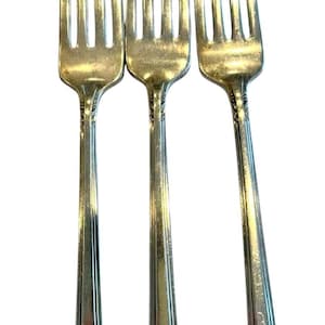 May include: Three silver-toned metal forks arranged vertically. Each fork features four long tines and a slender handle decorated with a raised floral pattern along the edges and a beaded border detail near the base of the handle.