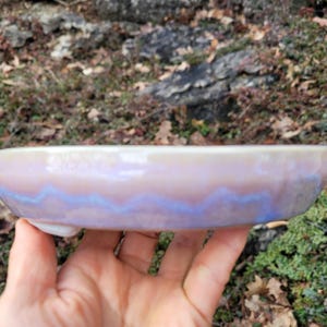 May include: A white ceramic mug with a black handle and the text "But First, Coffee" in a bold, black font. The mug is set against a blurred background. The mug appears to be approximately 10 cm tall.