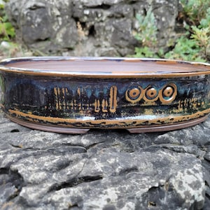 Peut inclure: Pot à bonsaï ovale fait à la main. Le pot en céramique présente un glaçage bleu foncé avec des accents bronze et des motifs décoratifs. Le bord et la base sont en bronze. Conçu pour la plantation de petits arbres.