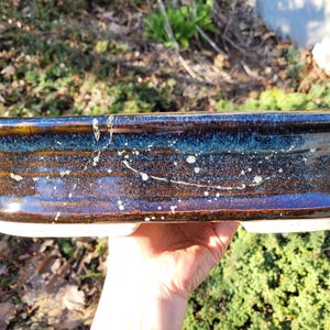 May include: A rectangular ceramic planter with a glossy, dark blue and brown glaze. The planter has a speckled pattern of white dots and a slightly raised rim. The base is a lighter, unglazed color.