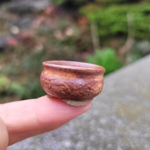 May include: A miniature brown ceramic bowl with a textured surface. The small bowl, about 2.5 cm in diameter, has a rounded shape and sits on a small, unglazed base. The bowl is likely for miniature plants or decorative purposes.