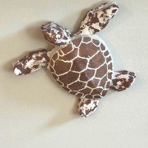 Könnte beinhalten: Dekorative Schildkrötenfigur mit braun-weiß gemustertem Panzer und Gliedmaßen. Der Schildkrötenpanzer weist ein detailliertes, geometrisches Design auf, und die Figur scheint aus einem strukturierten Material zu bestehen.