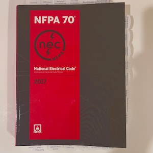 May include: A copy of the National Electrical Code, NFPA 70, 2017 edition. The cover is red with white text and a circular logo. The book has labeled tabs for easy reference, including Contents, Definitions, and Branch Circuits.