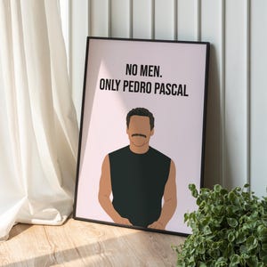 Puede incluir: Un cuadro enmarcado con el texto "NO MEN. ONLY PEDRO PASCAL" sobre una ilustración estilizada de un hombre con bigote. El cuadro tiene un fondo rosa y un marco negro. La obra de arte está apoyada contra una pared blanca.