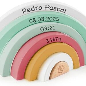 May include: A decorative wooden rainbow stacker featuring six nested arches in white, mint green, dusty rose, and mustard yellow. The arches are printed with the text Pedro Pascal, 08.08.2025, 03:21, and 3467g. The smallest center piece is natural wood.