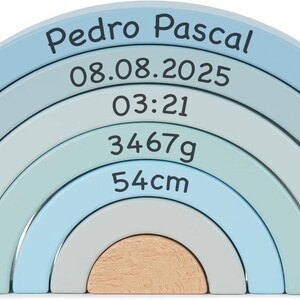 May include: A wooden rainbow stacker toy featuring five nested arches in shades of blue, light blue, and natural wood. The arches are printed with the text Pedro Pascal, 08.08.2025, 03:21, 3467g, and 54cm in a dark font across the curved surfaces.