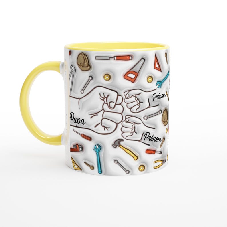 Puede incluir: Una taza de cer&aacute;mica blanca con asa e interior amarillos. La taza presenta un dise&ntilde;o de herramientas y pu&ntilde;os, con la palabra "Papa" y "Pr&eacute;nom" en texto negro. Las herramientas son de varios colores.