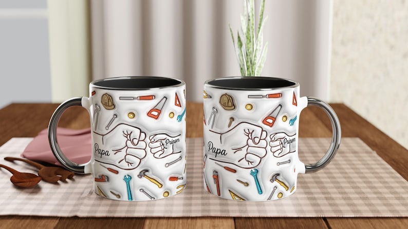 Puede incluir: Dos tazas de cer&aacute;mica blanca con bordes negros y asas plateadas. Cada taza presenta un dise&ntilde;o de herramientas, un pu&ntilde;o y la palabra "Papa". Las tazas est&aacute;n decoradas con ilustraciones de martillos, sierras y llaves.