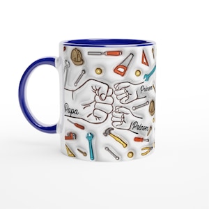 Puede incluir: Taza de cer&aacute;mica blanca con asa y borde azules. La taza presenta un dise&ntilde;o de herramientas y pu&ntilde;os, con las palabras "Papa" y "Pr&eacute;nom" impresas. Un gran regalo para un padre o abuelo.