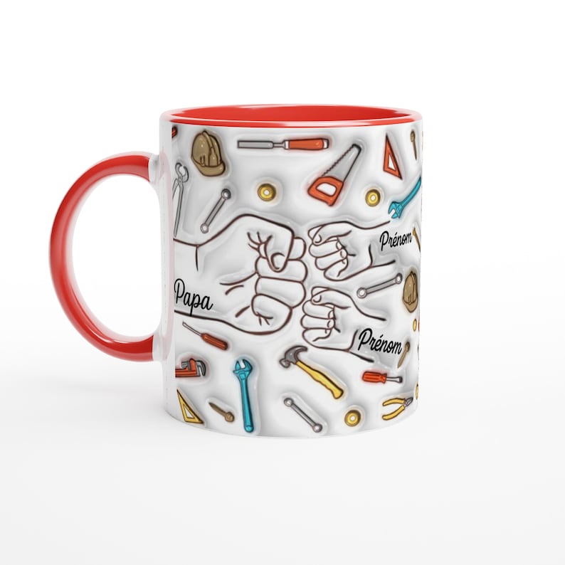 Puede incluir: Una taza de cer&aacute;mica blanca con asa e interior rojos. La taza presenta un dise&ntilde;o de herramientas y pu&ntilde;os, con las palabras "Papa" y "Pr&eacute;nom" en escritura negra. Las herramientas son de varios colores, incluyendo rojo, amarillo y azul.