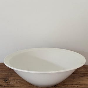 May include: A plain white bowl with a wide, flat rim and a smooth, rounded basin. The bowl features a clean, minimalist design with a consistent white finish throughout its interior and exterior surfaces, showcasing a simple and functional form.