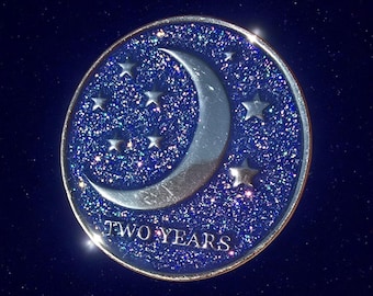 May include: A round, blue and silver commemorative coin with a crescent moon and stars design. The coin has a glittery background and the words "TWO YEARS" are printed at the bottom.