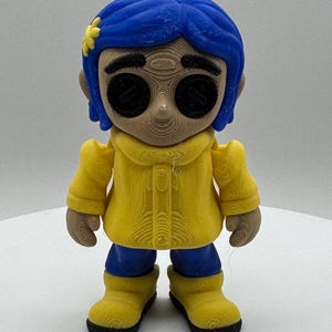 May include: A 3D-printed figurine of a character with blue hair, button eyes, and a yellow coat. The figurine has a flower in its hair and is wearing blue pants and yellow boots. The figure is standing on a white surface.