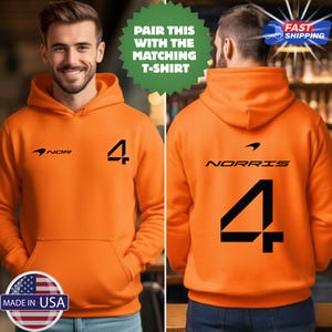 May include: Orange hoodie with a front kangaroo pocket. The front features the text "NOR" and the number "4" in black. The back displays "NORRIS" and the number "4". The hoodie has a hood and long sleeves. The text "PAIR THIS WITH THE MATCHING T-SHIRT" is also visible.
