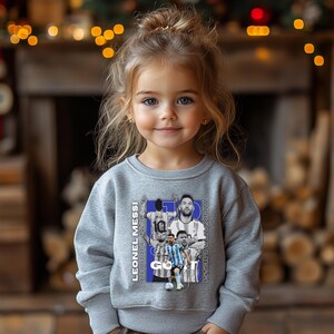 May include: A grey sweatshirt with a collage of Lionel Messi images and the text "LEONEL MESSI" and "ANKARA MESSI". The design includes the word "GO" in white. The sweatshirt is worn by a young child.